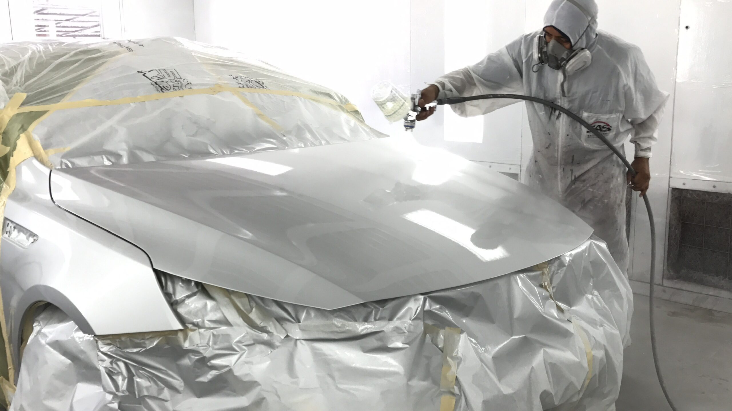 Automotive technician painting car frame in Covina Auto Body shop.